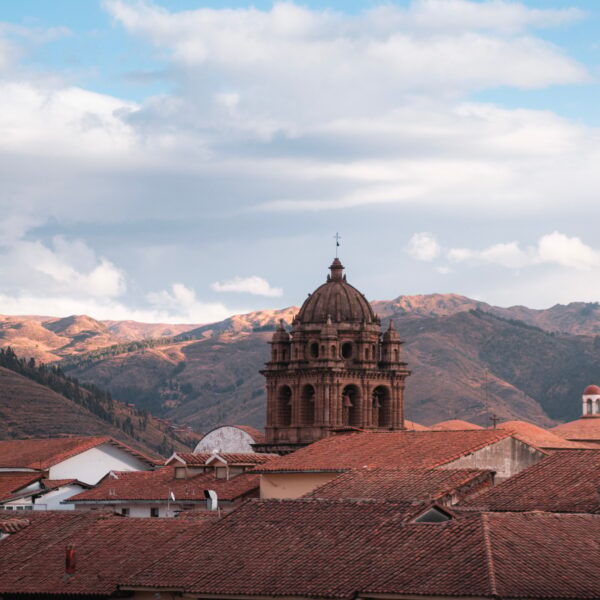 Church tower emerging from cusco rooftops with andes mountains in background