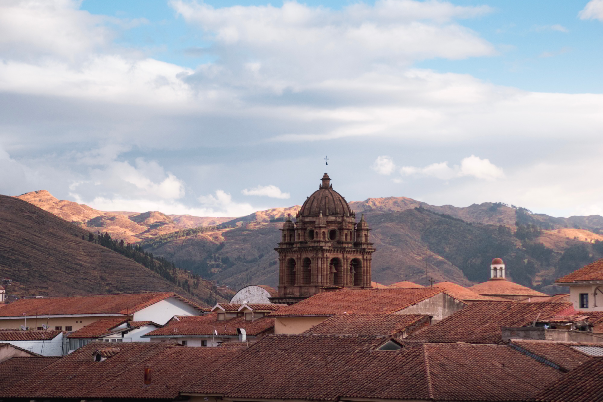 Church tower emerging from cusco rooftops with andes mountains in background